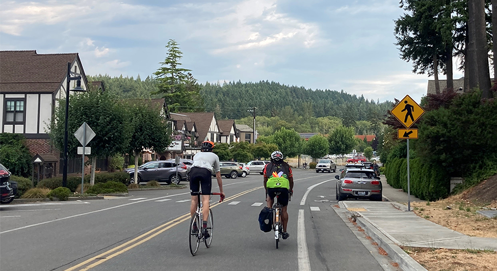 Two bicyclists descending a two-lane street, approaching a pedestrian crosswalk